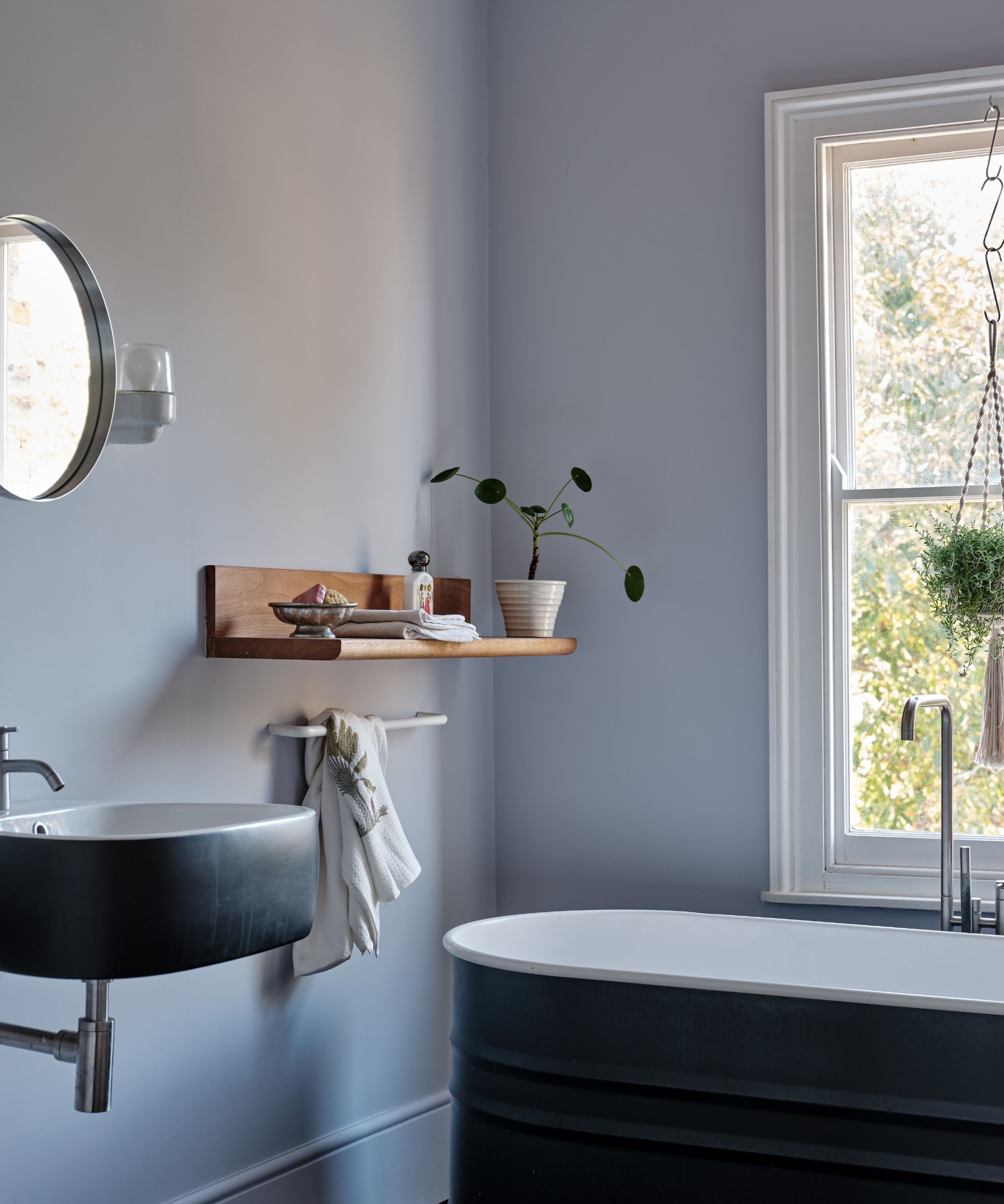 coin de la salle de bain avec murs gris-bleu glacé, bain foncé avec étagère en bois sur le mur par la fenêtre