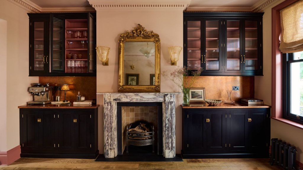5 choses à nettoyer en mai – celles-ci emballeront votre espace à temps pour l’été Veined marble fireplace in the middle of two built in kitchen cabinet unit. It's in a dark and moody utility room with dark academia feel, black cabinets, low lighting and gold and brass accents
