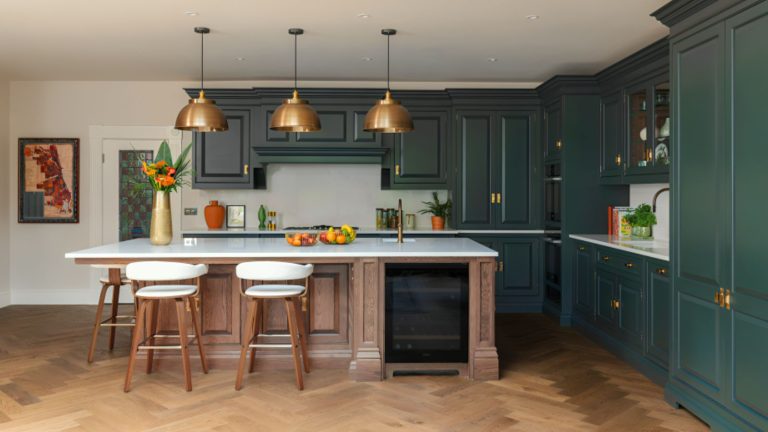 A traditional blue-green kitchen with a wooden island and white barstools. Three brass pendants above.