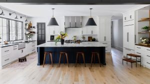 A white kitchen with a dark blue island topped with a marble countertop, with perimeter cabinets topped with granite countertops