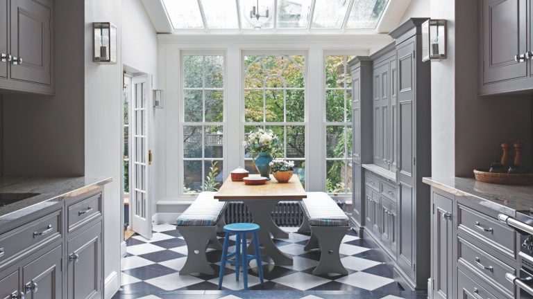 5 points négligés que vous oubliez de désencombrer – les hiérarchisez maintenant ou rencontrez des difficultés plus tard, avertissent les experts A black and white tiled kitchen with dark grey cabinets, a wooden dining table with grey benches, and large white windows.