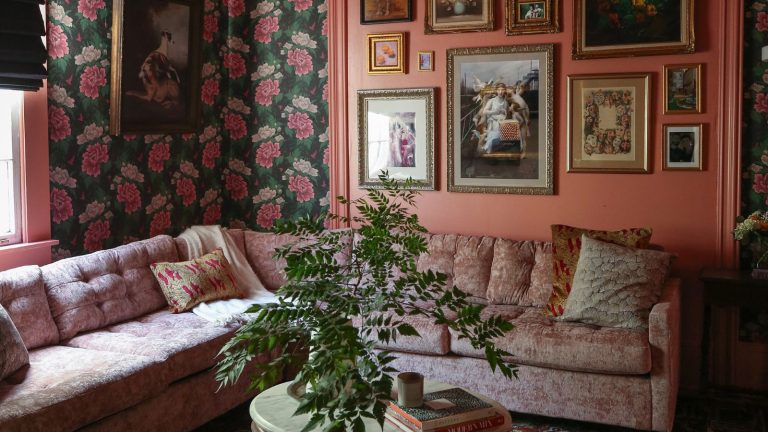 Trop occupé pour désencombrement? Le système d’amélioration incrémentiel crée un changement durable avec de petites actions quotidiennes, disons les pros A living room with floral wallpaper, a gallery wall, a dusky pink L-shaped couch, and a marble table with a plant and books on top of it