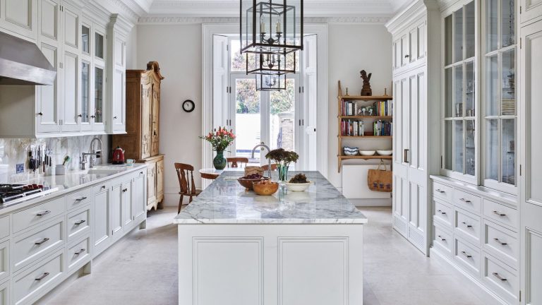 Cet organisateur de Joseph Joseph Joseph Cutlery est idéal pour réviser même les tiroirs de cuisine les plus désagréables – c’est tellement compact et respectueux du locataire A white kitchen with marble island, white and glass cabinets, and wooden shelves and dresser.