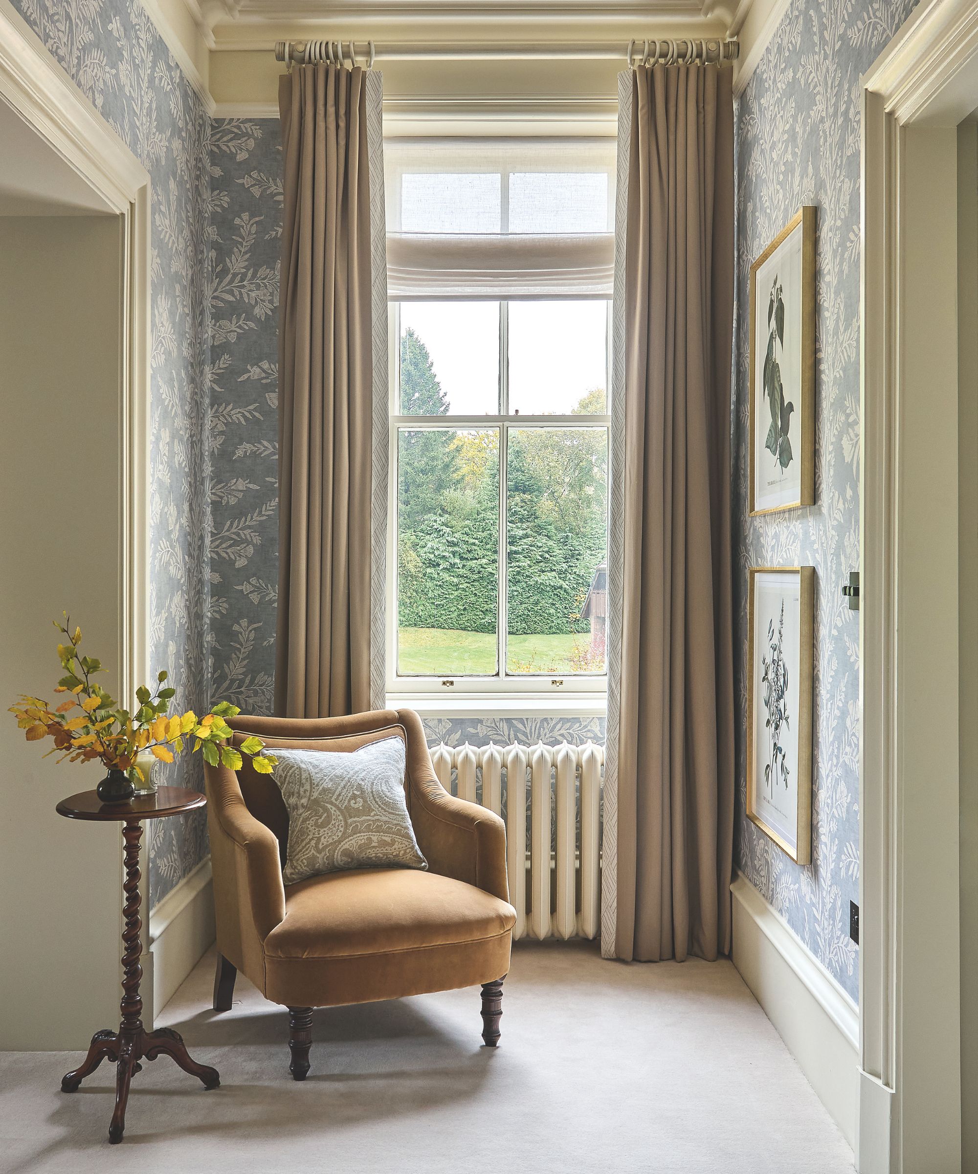 Entrée avec grande fenêtre avec rideaux beige, papier peint floral bleu et blanc, chaise orange et petite table d'appoint en bois