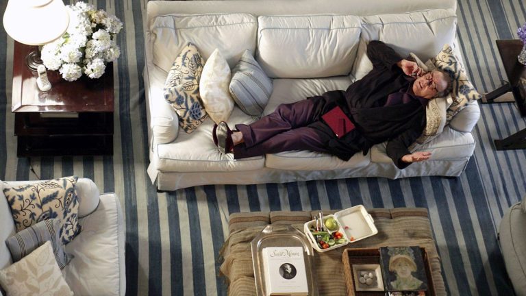 6 pièces vintage que nous avons repérées dans les films de Nancy Meyers qui ont inspiré un voyage dans la friperie still image from 'Somethings Gotta Give' 2003 movie by nancy meyers showing Jack Nicholson lying on a white linen sofa with a blue stripe carpet underneath, antique furniture and decor and a large hydrangea plant