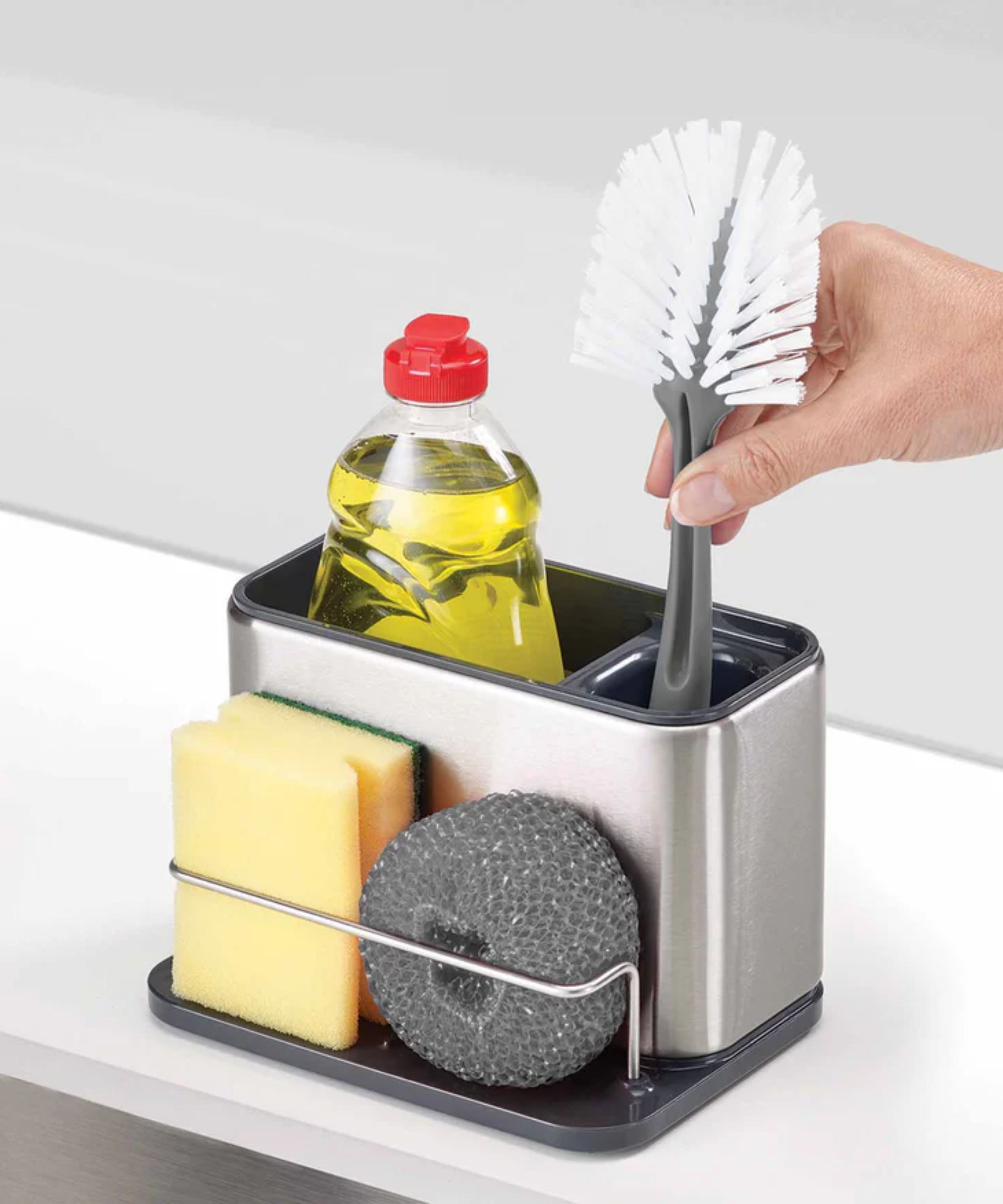Un lavabo argenté organisant un caddie avec du savon à vaisselle jaune, une brosse à nettoyer et des éponges à récurer.