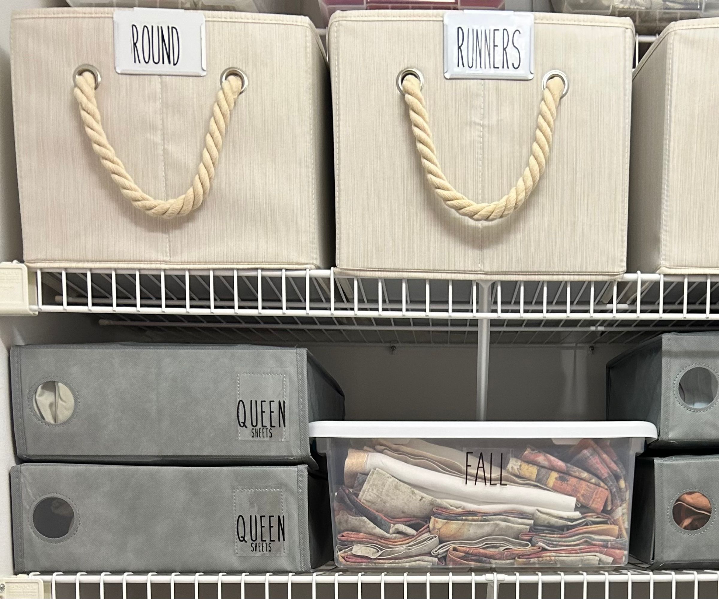 Boîtes de rangement de literie grise sur les étagères Wite, sous les paniers étiquetés en crème avec des poignées de corde.