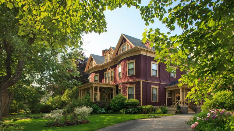 A large brick victorian home with a large front lawn and trees surrounding it