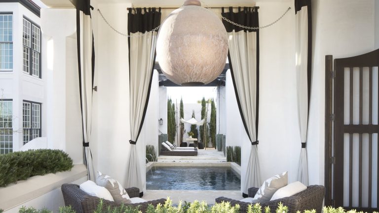 Non, les rideaux ne sont pas réservés à l’intérieur – voici pourquoi ajouter des rideaux à votre terrasse rendra votre espace extérieur instantanément plus luxueux A sheltered outdoor area with a spherical lampshade, garden furniture, and curtains with black trim
