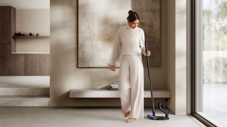 Person holding the Dyson PencilVac in sleek, modern, brown home with large abstract painting pictured behind, next to large window.