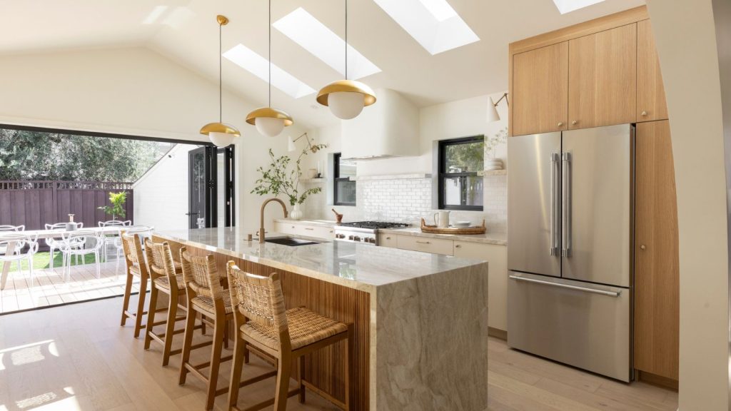 Époudeur d’air vs purificateur d’air – qui est mieux pour votre maison? Les professionnels du CVC et les experts de l’industrie révèlent la solution de nettoyage d’air la plus efficace Modern kitchen with large stainless steel fridge freezer, marble kitchen island with four rattan chairs, three golden hanging lights. Pictured in background is cooker, two small windows, white bricked tile splash wall, and outdoor area with table and chairs.