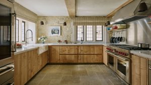 A Cotswolds kitchen with wooden cabinets, exposed stone walls, stainless steel appliances, and flagstone flooring