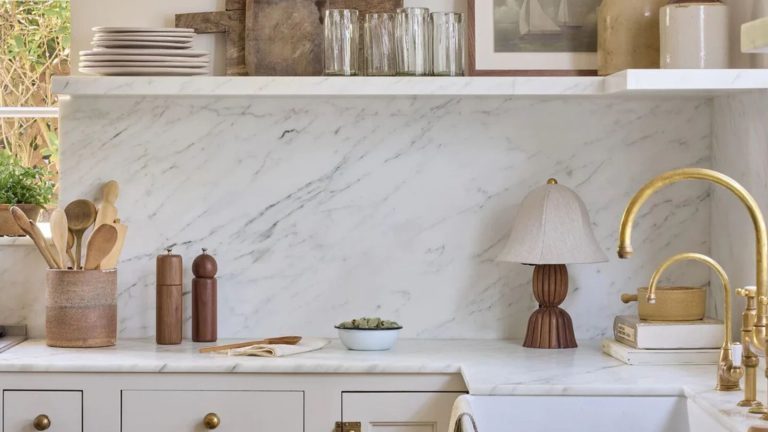 Cette cuisine tranquillement élégante mais charmante est une leçon de style vécu – et j’ai trouvé tous les accessoires de style vintage dont vous avez besoin pour recréer le look A kitchen with warm neutral cabinets and a marble countertop, backsplash, and shelf decorated with curated decor from Shoppe Amber Interiors