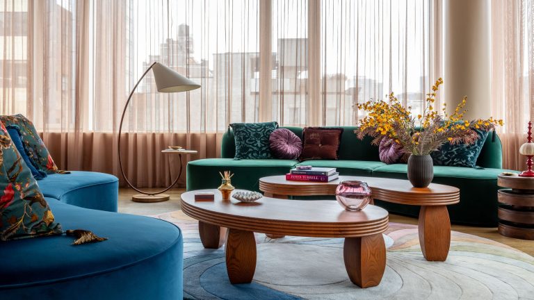Vous ne sauriez jamais que les joyaux hauts sont cachés dans cet appartement élégant mais éclectique de New York – mais le designer nous a laissé sur où acheter toutes les pièces clés A living room with curving blue sofas, beige curtains, long, oval coffee tables and a round carpet