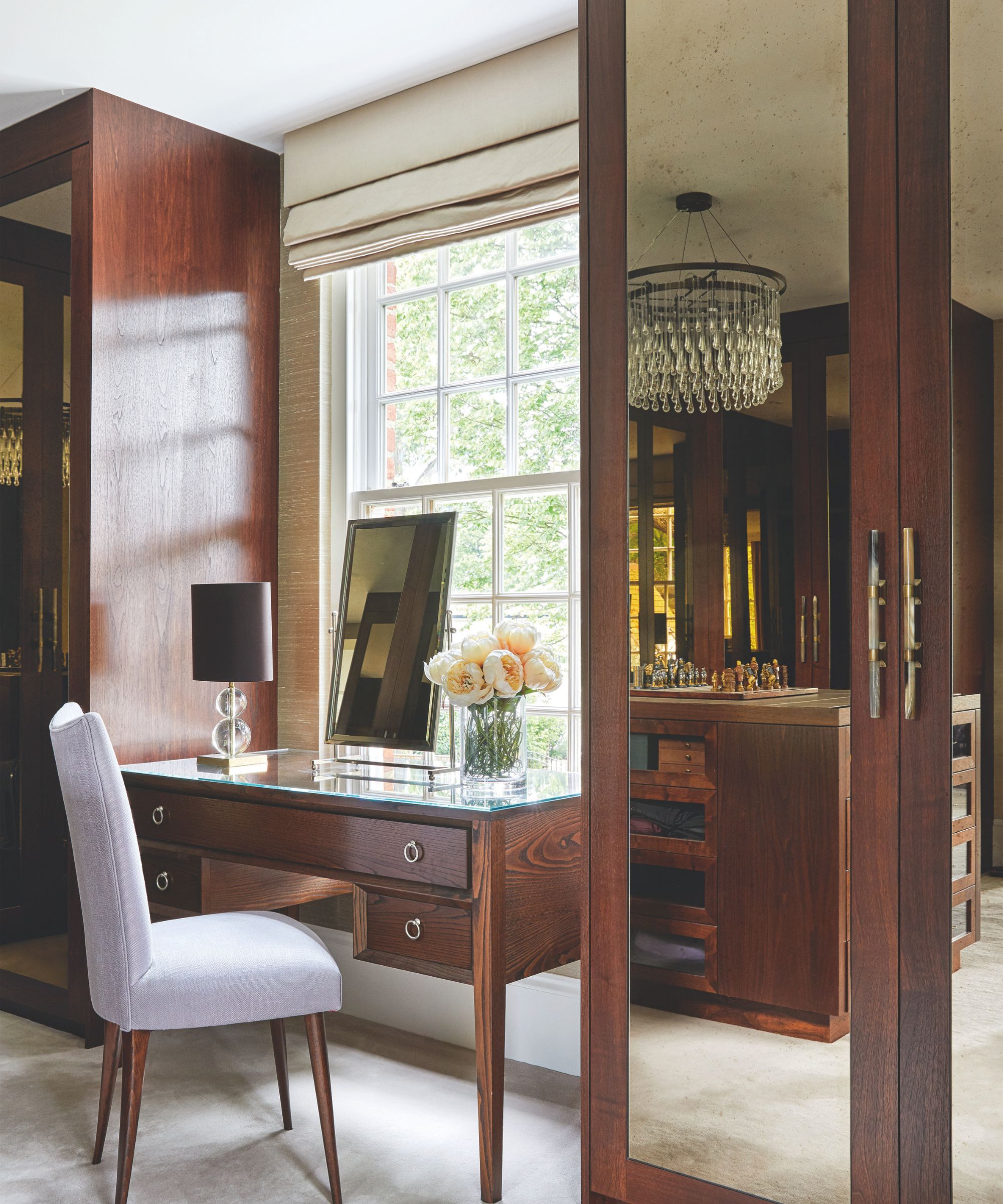 Claculteurs bruns en miroir dans la chambre avec une coiffure en miroir marron, une chaise blanche, un miroir et une grande fenêtre lumineuse avec des stores beige.