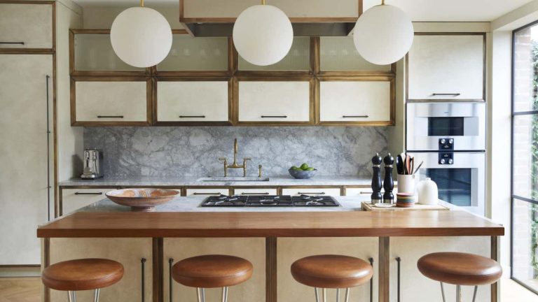 A neutral kitchen, with cream top cabinets and a brown wooden island. A grey marble back splash, and four brown leather bar stools.