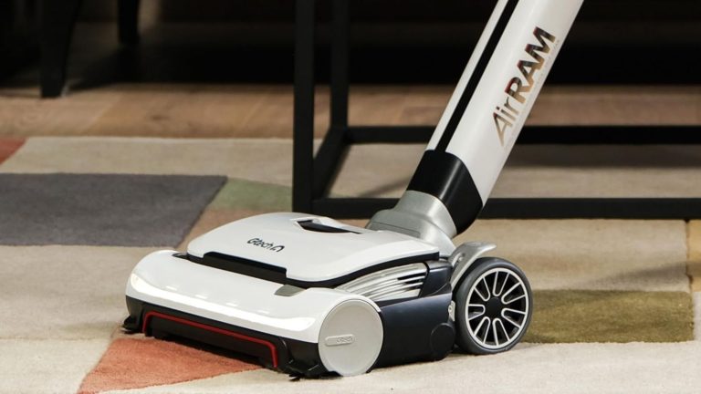 Gtech AirRAM 3 cordless vacuum cleaner on colorful, patterned rug in front of table legs.