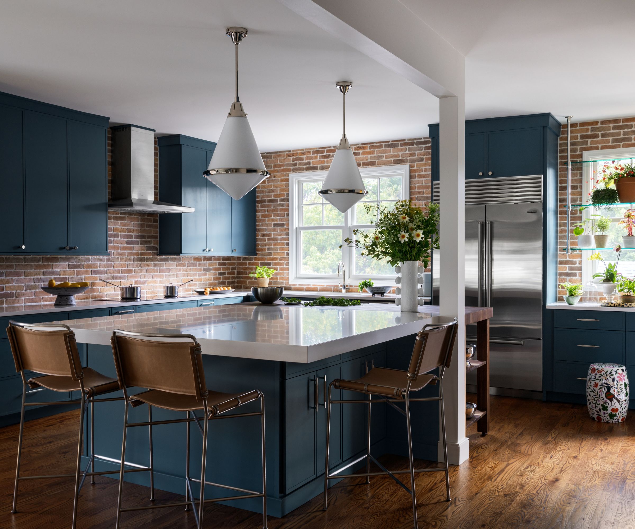 Cuisine avec armoires bleues, dosseret en brique et bloc de boucheurs en bois attaché à une île surmontée en marbre blanc