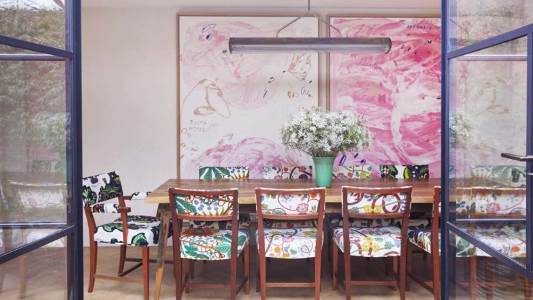 « C’est trompeusement simple mais étonnamment efficace » – comment la méthode de désencombrement du «point et fossé» lance la fatigue de la décision au trottoir A dining room with large pink swirl artwork on the walls. A long wooden rectangular dining table with colorful chairs around it. A large green vase of white flowers as a centrepiece.