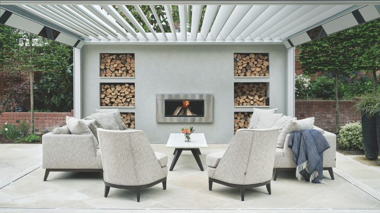 Ce ventilateur répulsif portable à 7 $ d’ALDI est un incontournable pour l’été – les entomologues révèlent comment l’utiliser pour une « zone sans bugs personnelle ‘non toxique’ ‘ A large concrete patio with white upholstered chairs and sofa with white table, large white awning and central log burner with recessed wood storage