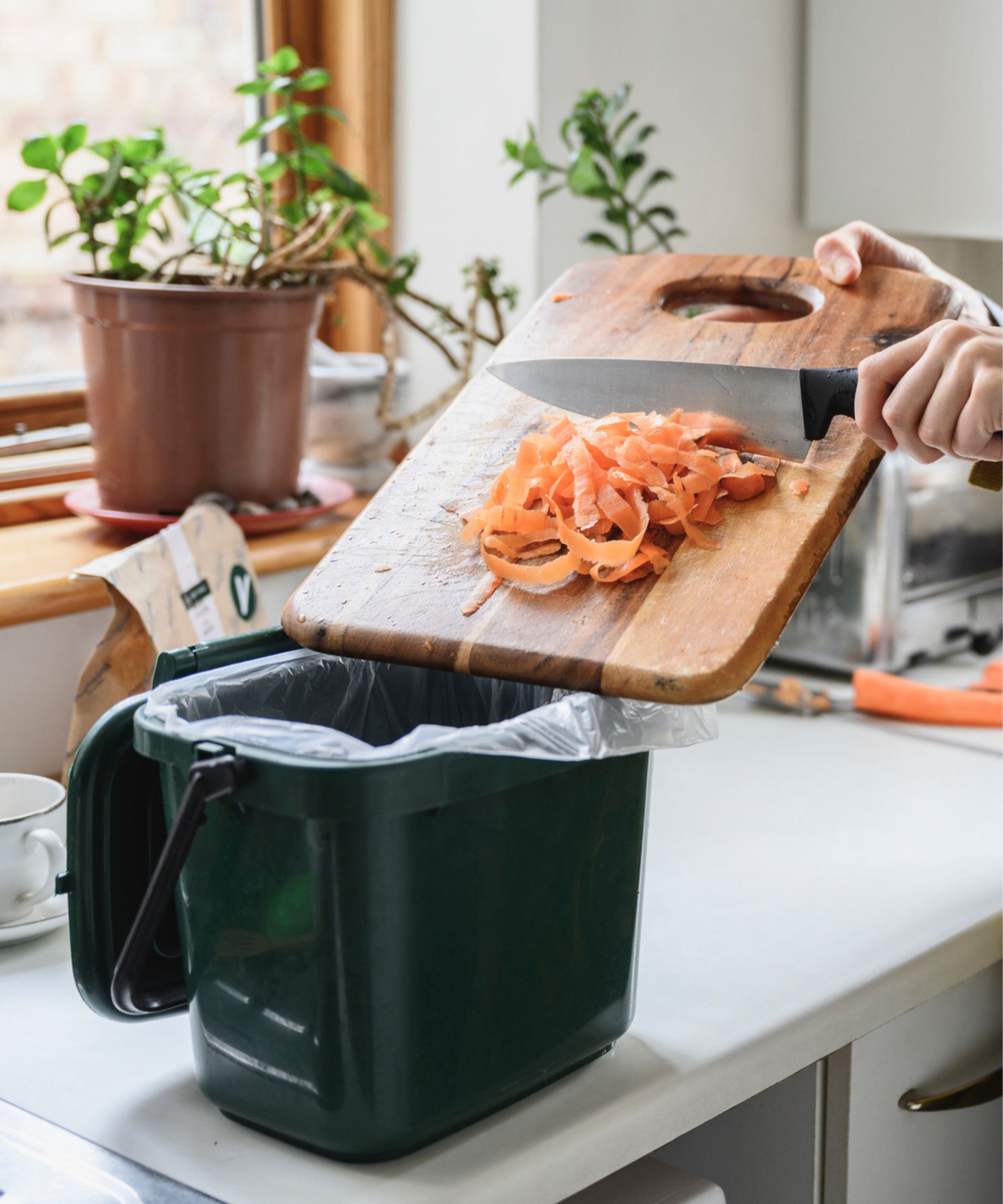 Un bac à compost vert foncé avec des peilles de carotte sur un panneau de coupe en bois qui y est gratté