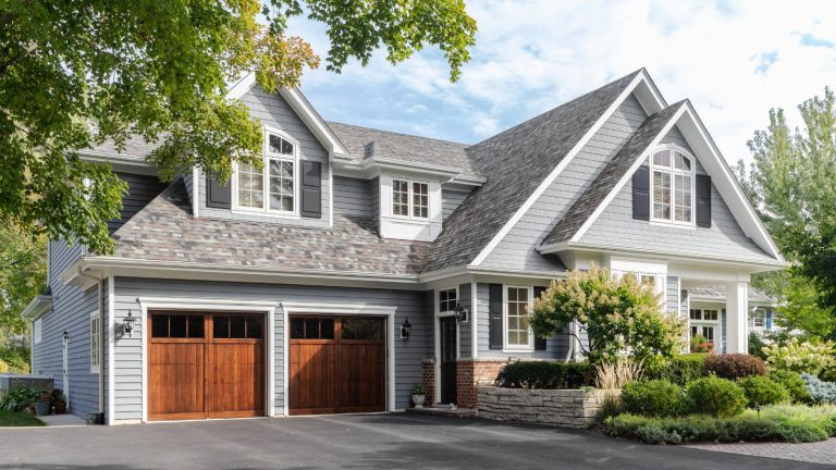 Comment emballer un kit de préparation aux ouragans de bricolage – 10 ‘essentiels « à prépper A large grey and white modern farmhouse with two wooden garage doors, and beautiful landscaping.