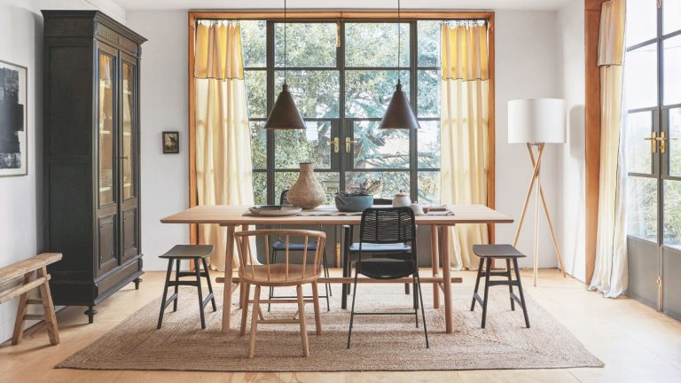 Quelle est la règle 20/20 pour le désencombrement? Nos experts organisationnels expliquent tout ce que vous devez savoir Bright and airy dining area with floor-to-ceiling windows, a wooden dining table, mismatched chairs and a large jute rug. To the left is a large black cabinet, and to the right is a tall wooden lamp with white lampshade.