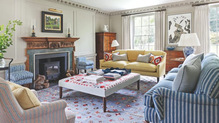 Traditional living room with large windows a yellow couch and striped couches positioned around a upholstered coffee table