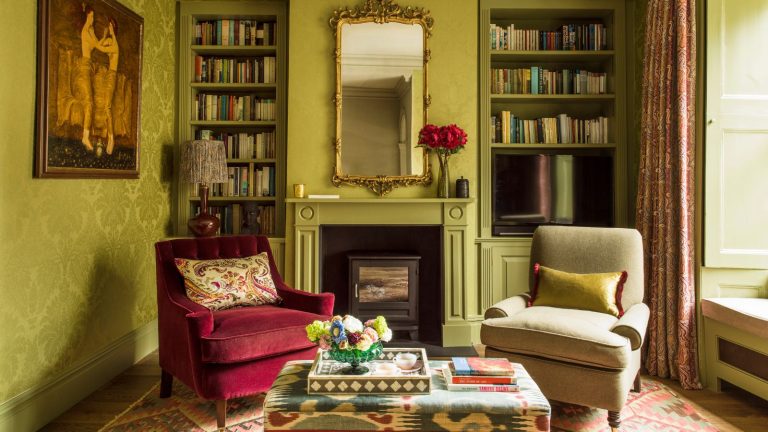 Green grand living room with armchairs, ottoman, gold mirror, fireplace and antique art and bookcases