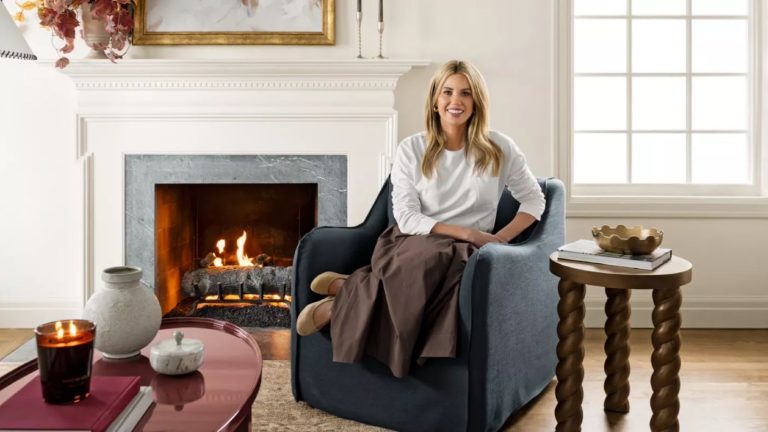 Ma maison est remplie de trouvailles économes, mais ce tableau cible Shea McGee X inspiré de vintage offre le même look pour moins – et il est actuellement de 100 $ de rabais Designer Shea McGee photographed for her Target 2025 collection sat on a navy slipcovered armchair beside a fireplace with a wooden turned side table and a lacquered red coffee table
