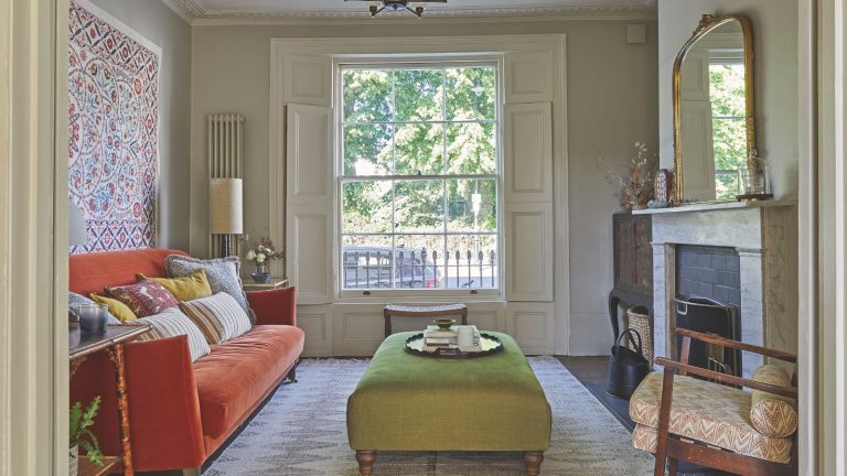 Traditional living room with orange sofa and marble fireplace with a green ottoman and a wall hanging