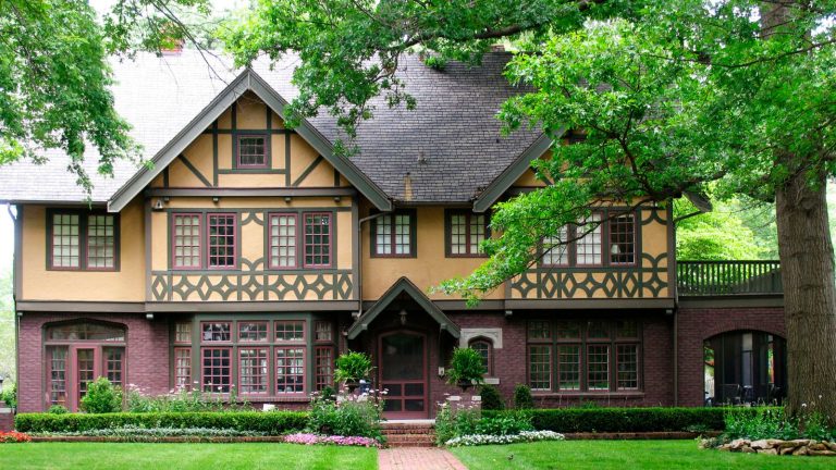 Qu’est-ce qu’une maison de style Tudor? Tout ce que vous devez savoir sur ce style architectural classique Tudor revival style house painted yellow and red with large tree and lawn
