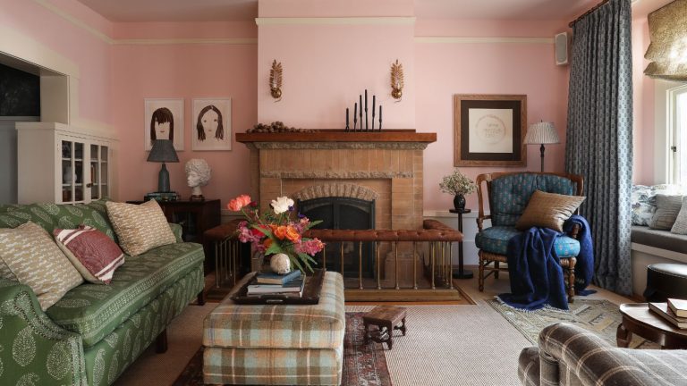 Je n’ai jamais pensé que je décorerais avec du rose et du brun – mais les designers m’ont convaincu que c’est la combinaison de couleurs la plus sophistiquée pour 2025 et au-delà traditional cozy living room with pink walls, green sofa, brick fireplace, and plaid ottoman