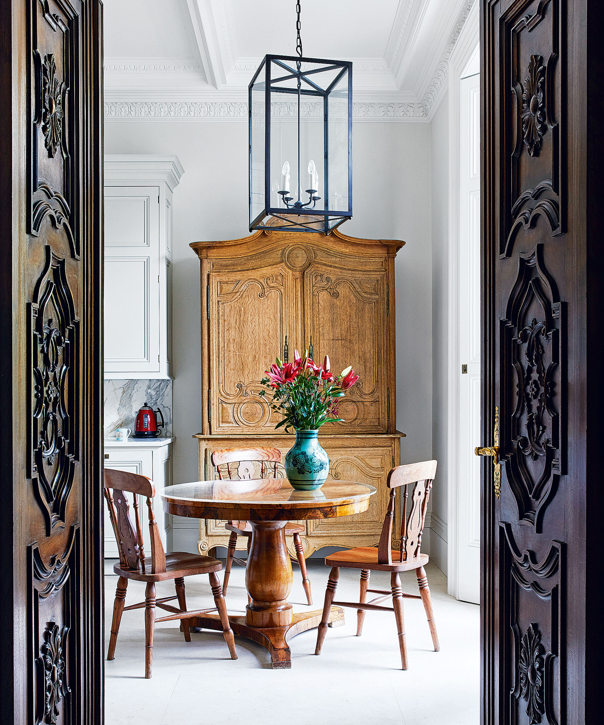 En regardant à travers des portes en acajou ornée ouvertes dans la cuisine avec table ronde de style country et chaises et commode de noix