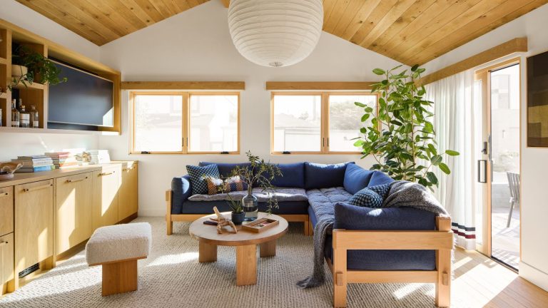 Cet achat approuvé par le designer inattendu et abordable m’a sauvé de maîtrise de mon canapé – et c’est mon piratage préféré pour les ménages occupés modern coastal style living room with a wooden panelled ceiling and large paper rice ceiling glob lampshade and navy sofa with topper