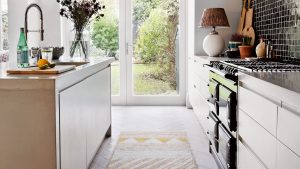 Kitchen with wooden floor, white fitted cabinets and kitchen island, glass door to garden.
