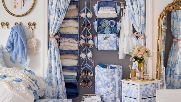 LoveShackFancy ne fait pas seulement des robes mignonnes, ils font aussi le décor de dortoir le plus rêvé – la nouvelle collaboration de grange de poterie est là pour transformer le plus facial des dortoirs en quelque chose de fantaisiste Dorm room decorated with pieces from the LoveShackFancy x Pottery Barn collaboration. These items include curtains, a storage cart, laundry hamper, and hanging closer organizers, all in a blue damask pattern. Gold details, including a vintage light-accented ornate floor mirror, bow shaped hooks, and framed art work, accent the scene.