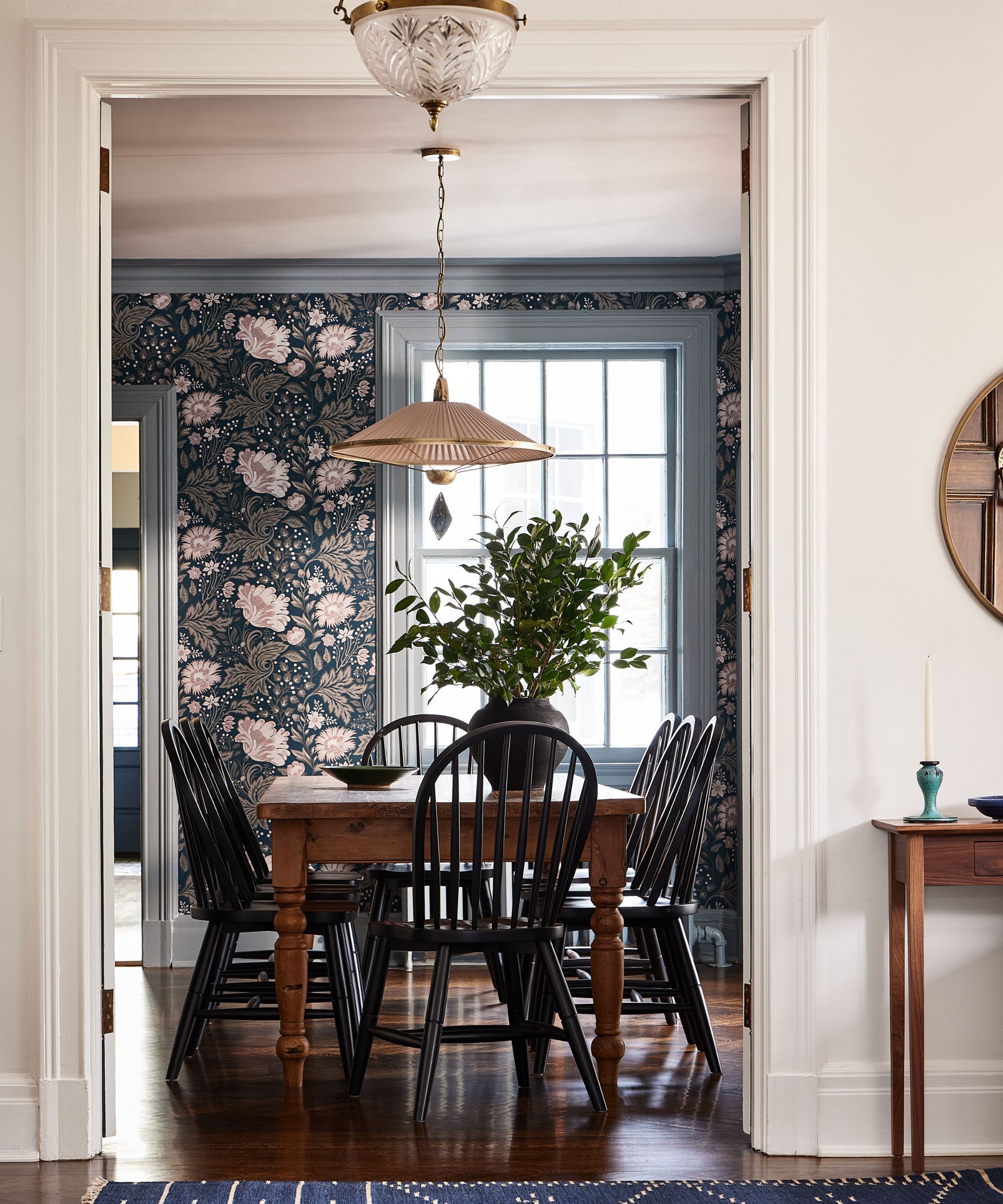 Couloir regardant dans la salle à manger avec du papier peint à floral, table à manger en bois et chaises et léger