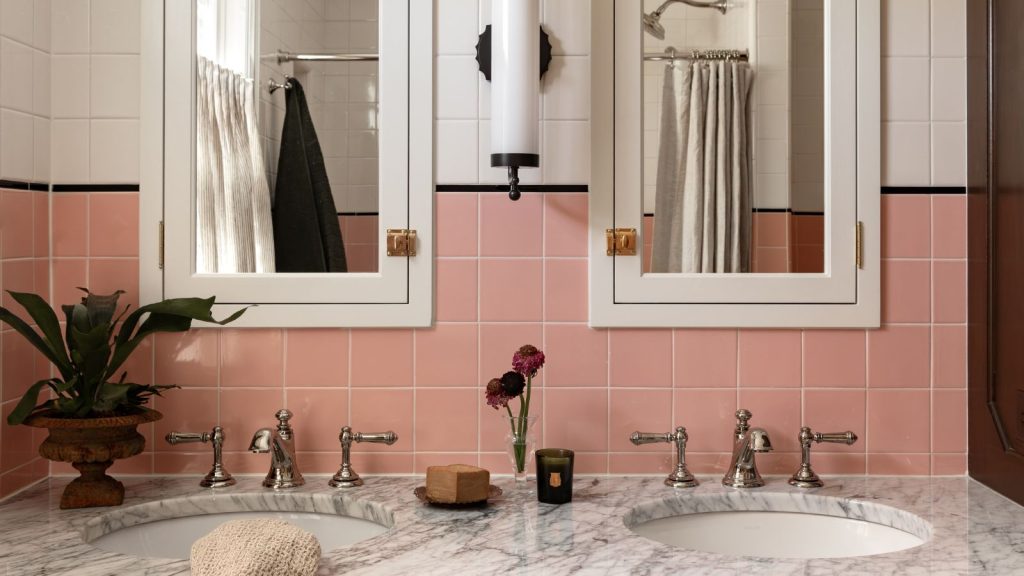 bathroom with a marble topped double vanity with nickel hardware and a pair of mirrored bathroom wall cabinets with pink square wall tiles and a black border between white tiles above