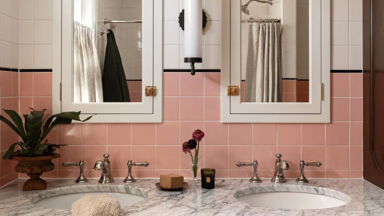 Cette couleur confiante des années 40 Minneapolis Remodel mélange la couleur saturée et les touches personnalisées réfléchies pour créer des pièces qui se sentent originales – mais mieux bathroom with a marble topped double vanity with nickel hardware and a pair of mirrored bathroom wall cabinets with pink square wall tiles and a black border between white tiles above