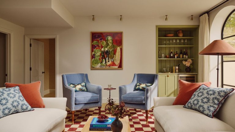 Cette table console Amazon Compacte de moins de 100 $ est la Pop audacieuse que ma maison neutre avait désespérément besoin – et c’est la preuve que la théorie rouge inattendue a vraiment des jambes neutral living with a green painted home bar in the corner, beige sofas with red and blue cushions, a red checkerboard rug, and blue arm chairs