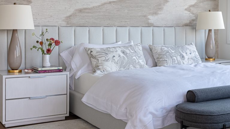 Light, airy bedroom featuring an oversized channel tufted headboard flanked by two nightstands with glossy-based table lamps.