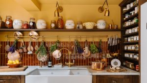 « J’ai l’impression que ce sont les étagères de ma vie » – comment le chef Clodagh McKenna a transformé une cuisine sombre en un espace chaleureux et rempli de personnalité qui équilibre l’experte de la fonctionnalité et du style vécu Clodagh McKenna's kitchen with yellow walls, burgundy backsplash tiles, marble countertops, and wooden open shelved displaying collected kitchenware and decor