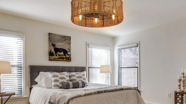 Fandeliers m’a rappelé ma maison d’enfance des années 90 – mais dans une tentative désespérée d’essayer de refroidir mon petit appartement, j’ai trouvé ce fandlier de rotin chic qui est élégant et fonctionnel Gray bedroom with rattan light, dog print above the bed and gray headboard