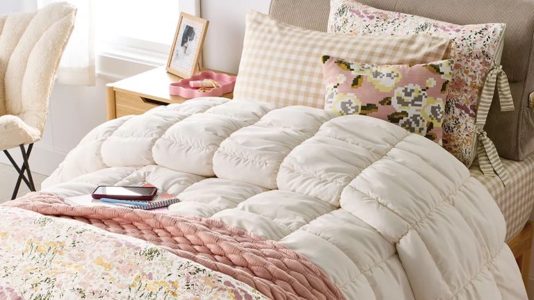 J’étais connu au collège pour mon dortoir incroyablement décoré – si la nouvelle collection de dortoirs de Target était disponible pour moi, c’est ce que j’aurais acheté Target dorm essentials, including a cream tufted comforter, blush and floral throw blankets, and gingham sheets, all styled on a twin sized bed next to a window