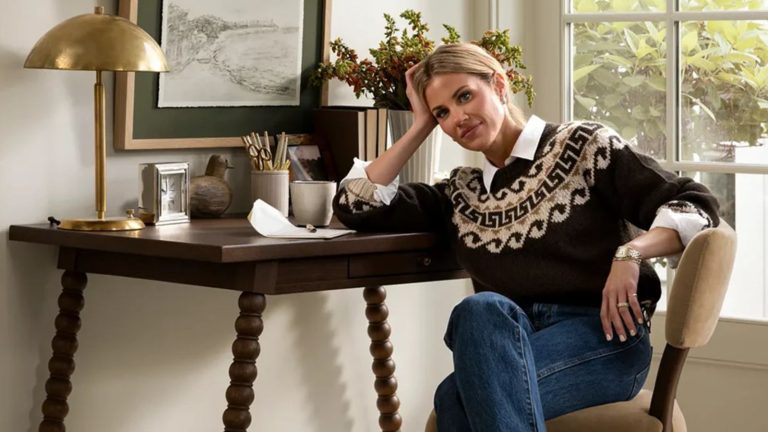 Vous cherchez à redécorer votre espace de sommeil? Shea McGee partage ses 3 conseils de conception pour créer une chambre «organisée et belle» interior designer shea mcgee photographed for the mcgee and co fall collection 2025 sat by a bobbin dark wood desk on a neutral chair wearing jeans and a knitted jumper