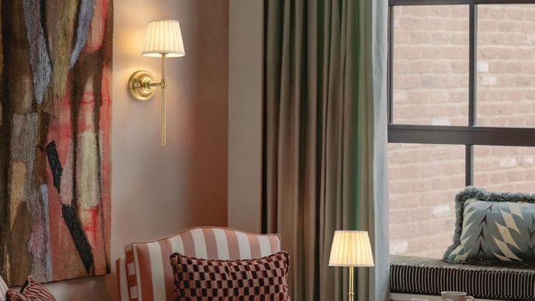 Je n’ai jamais pensé que je pouvais avoir des appliques de style hôtelier en tant que locataire – puis j’ai trouvé cette paire Amazon de 60 $ et il n’y a pas de fils laids en vue Amazon hotel style cordless wall light with a pleated fabric shade illuminating an art-filled livng room with a striped accent chair