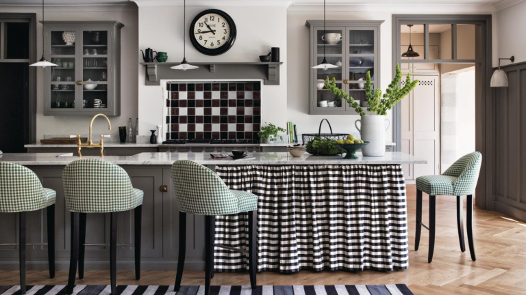 J’ai demandé aux concepteurs de partager les meilleures choses qu’ils ont achetées pour leurs cuisines en 2025 – voici les produits héros qu’ils jurent par a kitchen with a black and white printed counter skirt, green barstools, gray cabinets, and a vase of green plants on the counter