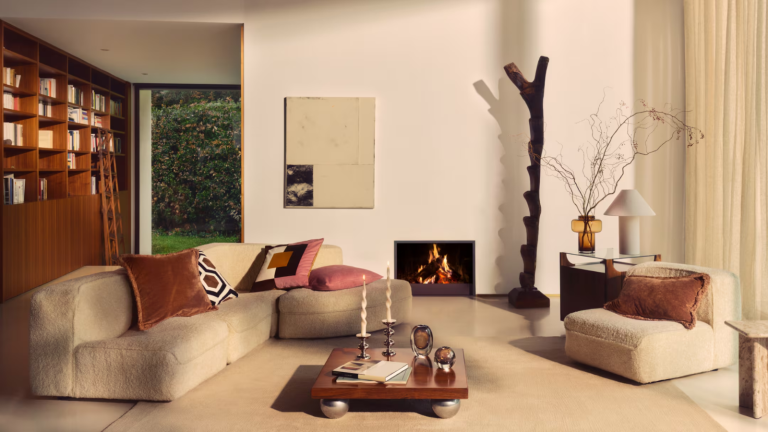 Selon la nouvelle collection des années 70 de H & M Home, l’élégance est l’ambiance de l’automne – si vous aimez le décor saisonnier sophistiqué, c’est la goutte pour vous a living room with low profile furniture, a wooden coffee table, a fireplace, lots of pillows, and a bookshelf against the left wall