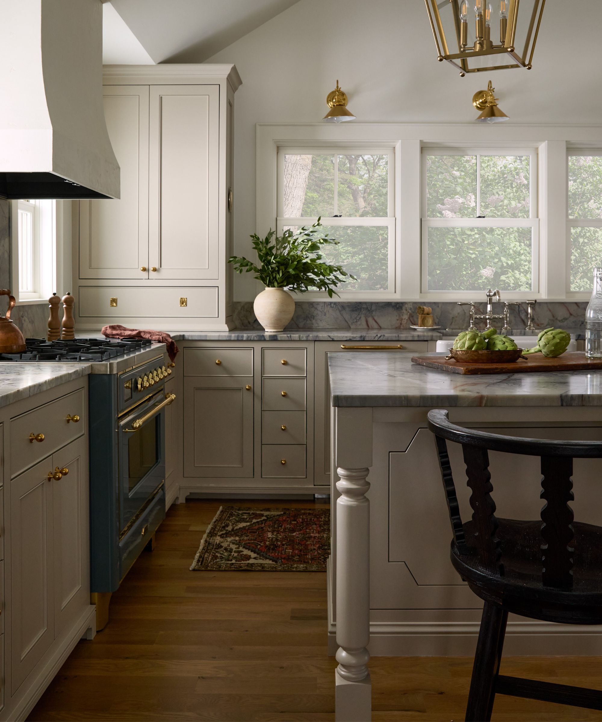 Cuisine neutre et terreuse avec de grandes fenêtres donnant sur le lac, une grande hotte en plâtre et des comptoirs en marbre bleu